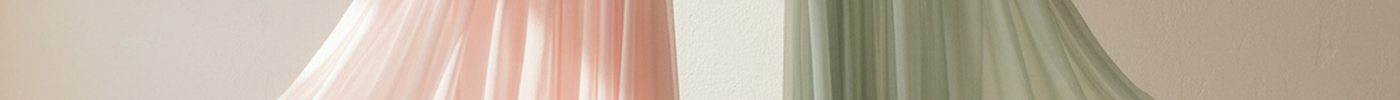 Zwei Chiffonkleider in Rosa und Salbeigruen haengen im Tageslicht, der Stoff faellt leicht
